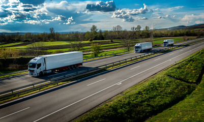 Highway transportation scene with three white transportation trucks in line on a rural highway...