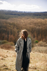 young girl in a long coat in the mountains. A girl walks on top of a mountain.