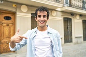 Young handsome caucasian man at outdoor person pointing by hand to a shirt copy space, proud and confident © Asier
