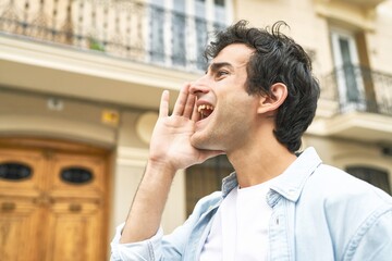 Young handsome caucasian man at outdoor shouting and holding palm near opened mouth.