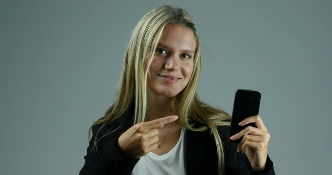 Young blond enthusiastic woman points to smartphone