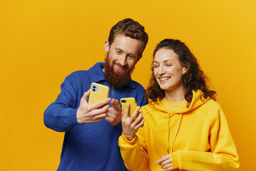 Man and woman couple smiling merrily with phone in hand social media viewing photos and videos, on yellow background, symbols signs and hand gestures, family freelancers.