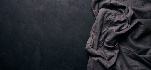 Folded black linen linen kitchen towel on a black background, top view. Copy space