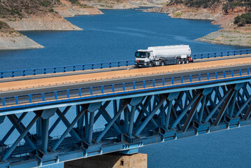 Fuel tanker truck driving over a bridge over a blue water swamp.