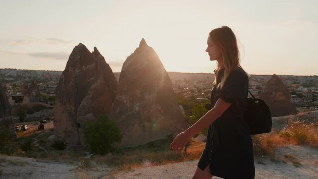 Side-view of beautiful thoughtfull young tourist woman walking on top of hill with beautiful view of countryside in Cappadocia Turkey