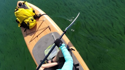 Woman on SUP board exercising at sea water. View from above. Special equipment such as seating chair and wet suit on paddleboard. Training and sport on paddle SUP board at sunny summer day.