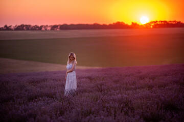 Fototapeta na wymiar Young blonde woman stands in purple field at sunset in the bright rays of sun. Travel in countryside. Allergy concept. Sunset sky. Carefree girl with long healthy hair. human countryside lifestyle