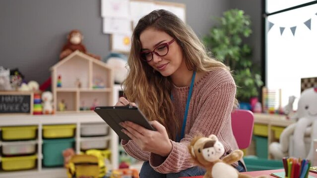 Young beautiful hispanic woman preschool teacher smiling confident using touchpad at kindergarten - Powered by Adobe