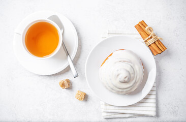 Cinnamon roll bun with cream glaze with cups of tea