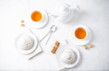 Cinnamon roll bun with cream glaze with cups of tea