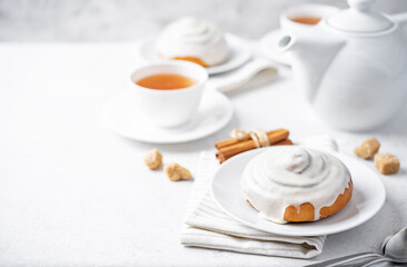 Cinnamon roll bun with cream glaze with cups of tea