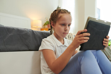 Emotional preteen girl watching tv show or animated cartoon on tablet computer