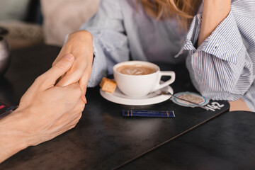 Female palm in the hand of man, at a table with coffee. Psychological support, romantic date concept. Couple having a coffee time while holding hands. Couple drinking coffee at cafe restaurant.