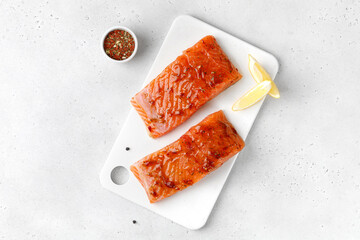 Marinated Salmon with sauce, red marinade, spicy. Fish steaks, slices. Raw uncooked salmon fillet fish with lemon and pepper on white cutting board and grey background.