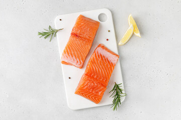 Salmon. Fish steaks, slices. Raw uncooked salmon fillet fish with rosemary, lemon and pepper on white cutting board and grey background.