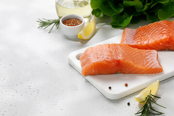 Salmon. Fish steaks, slices. Raw uncooked salmon fillet fish with rosemary, lemon and pepper on white cutting board and grey background.