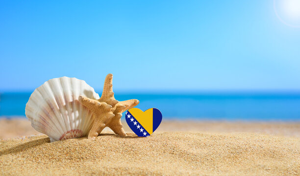 Beautiful beach in Bosnia and Herzegovina. Flag of Bosnia and Herzegovina in the shape of a heart and shells on a sandy beach.