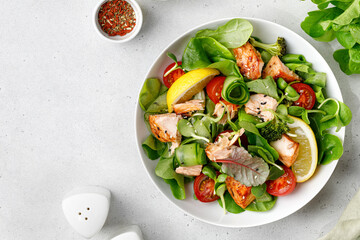 Healthy salad with pieces of baked salmon and green lettuce and tomatoes isolated on white background with clipping path. Fresh diet dinner meal. Fish summer salad. Vitamin food concept.