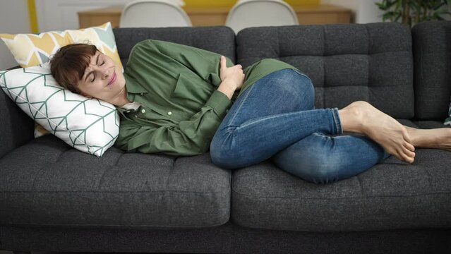 Young caucasian woman suffering from period pain lying on sofa at home