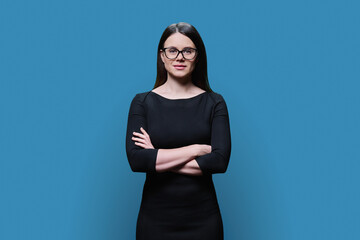 Fototapeta premium Young woman in glasses in black dress posing on blue background