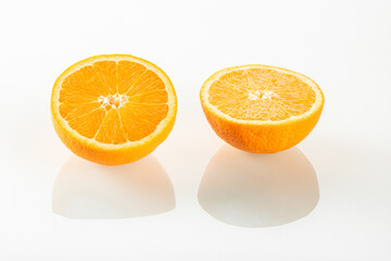 Two halves of an orange with reflection on a white mirror background