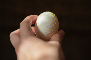 chicken egg in hand on a dark background. Easter. yellow mesh, decoration.
