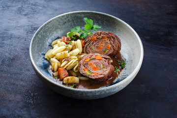 Traditionelle slow cooked deutsche Wagyu Rinderrouladen mit Gnocchetti-Sardi Nudeln in würziger Bratensoße als close-up auf einem Nordic Design Teller 