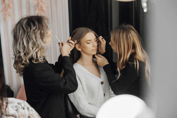 The face of a beautiful young woman. The process of creating hair and makeup. Beautiful hands in the process of work. White and black clothes. Three women with blond hair