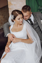 the bride and groom are sitting on a sofa against the background of green windows. Stylish bride and groom. Wedding photo. easy atmosphere