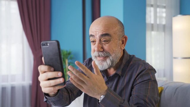 Happy old man talking facetime on the phone. 
Emotional old man is on the phone with his relatives facetime.
