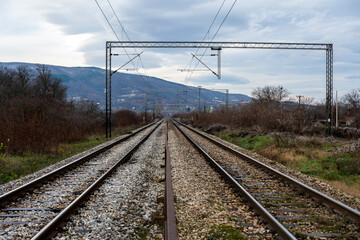 Infrastructure development project with laying of railway tracks equipped with overhead electric poles in parallel to high powered supply lines in dry terrain during summertime