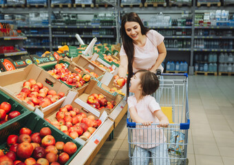 Family in the supermarket. young mother and her little daughter are smiling and buying food. Healthy food concept. mom and daughter buy vegetables and fruits in the supermarket