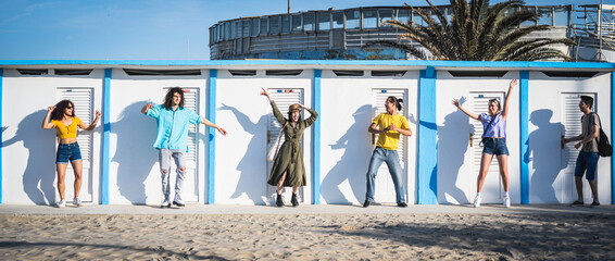 Six diverse people dancing in front of beach cabin, travel summer concept