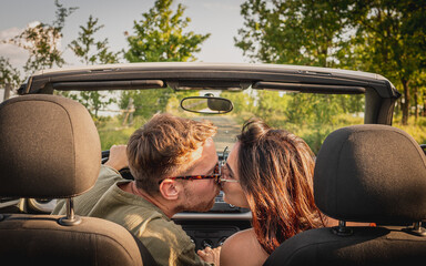Rear view, young couple kissing in a convertible car, happy beautiful couple in love kissing in a...