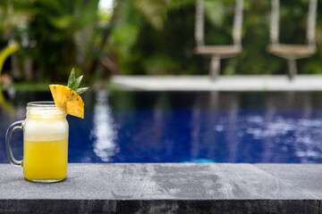 Fresh pineapple juice on swimming pool ledge on tropical paradise vacation resort. Copy space. No...