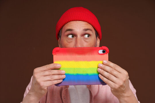 Gay man depicted feeling ashamed sexual orientation online, looking out with fear over tablet LGBT coloring. man in digital world represents negative emotions associated with secrecy and hidden