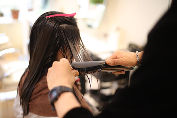 	女性の髪にヘアアイロンをかける男性美容師