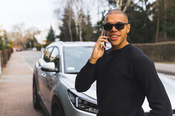 young businessman talking on the phone in the street, medium shot a silver car. High quality photo