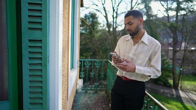 Person looking at smartphone device screen standing outside in balcony. An Arab Middle Eastern young man using phone