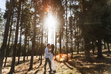 Obraz premium Stylish model couple in white clothes kissing at sunset in the forest. A girl hugs her husband, hair blowing in the wind. Wide angle photo