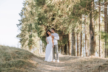 Stylish model couple in white clothes kissing at sunset in the forest. A girl hugs her husband, hair blowing in the wind. Wide angle photo