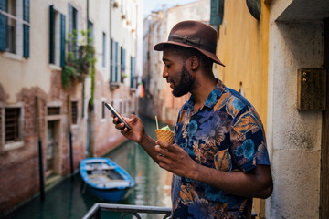 A tourist uses his smartphone while on holiday in Venice, stylish man with ice cream