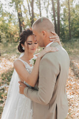 Naklejka premium Wedding portrait photo. Groom in a light suit. The bride and groom are standing in the forest embracing. Beautiful makeup and hair. Couple in love. Summer light. The shadows