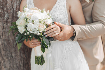 Photo of a wedding bouquet of white flowers and greenery in the hands of the bride and groom. The...