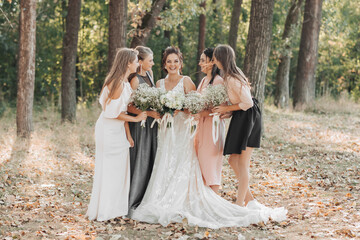 Wedding photo in nature. The bride and her bridesmaids are standing in the forest smiling, holding...