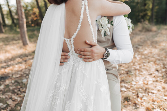 Wedding photo in nature. The bride hugs the groom. Groom's hands on the bride's waist. times Beautiful shoulders of the bride. Details