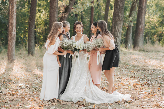 Wedding photo in nature. The bride and her bridesmaids are standing in the forest smiling, holding their bouquet and looking at the bride. Happy wedding concept. Emotions. girls