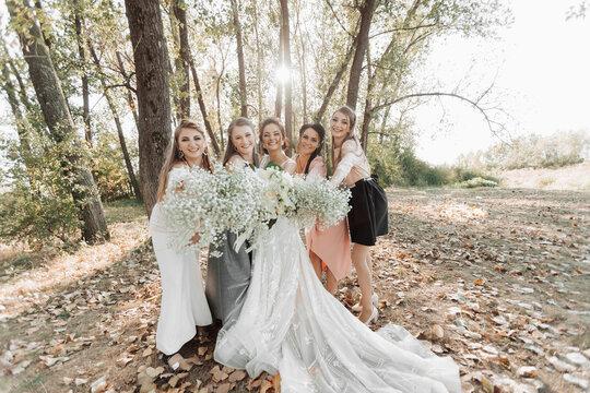 Wedding photo in nature. The bride and her bridesmaids are standing in the forest smiling, holding their bouquet and looking into the camera lens. Happy wedding concept. Emotions. girls