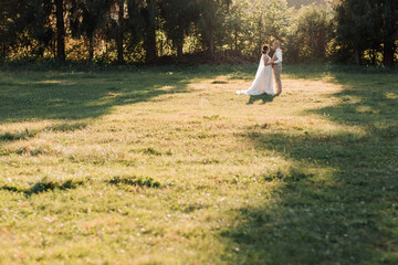 Happy bride and groom are standing on the field, looking at each other, behind them are big Christmas trees. Beautiful light that illuminates the bride and groom. Wedding photo. wide angle