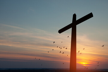 Christian cross with flying birds at sunrise. Resurrection of Jesus. Concept photo.